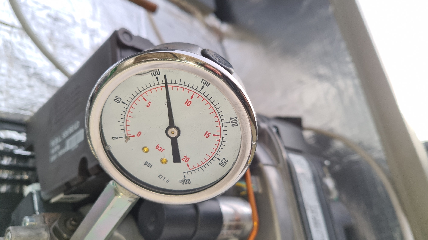 A pressure gauge reading in bar and psi, fitted to an oil burner pump during a service